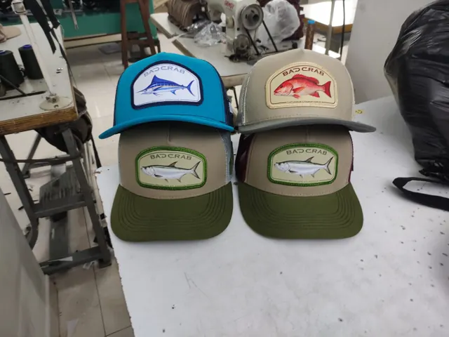 Cuatro gorras trucker con parche de pescado sobre la mesa de trabajo de CIJ Gorras