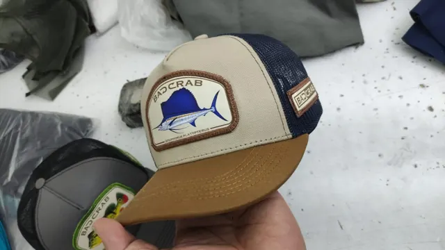 Gorra trucker beige con malla azul marino, visera camel y parche de pez vela