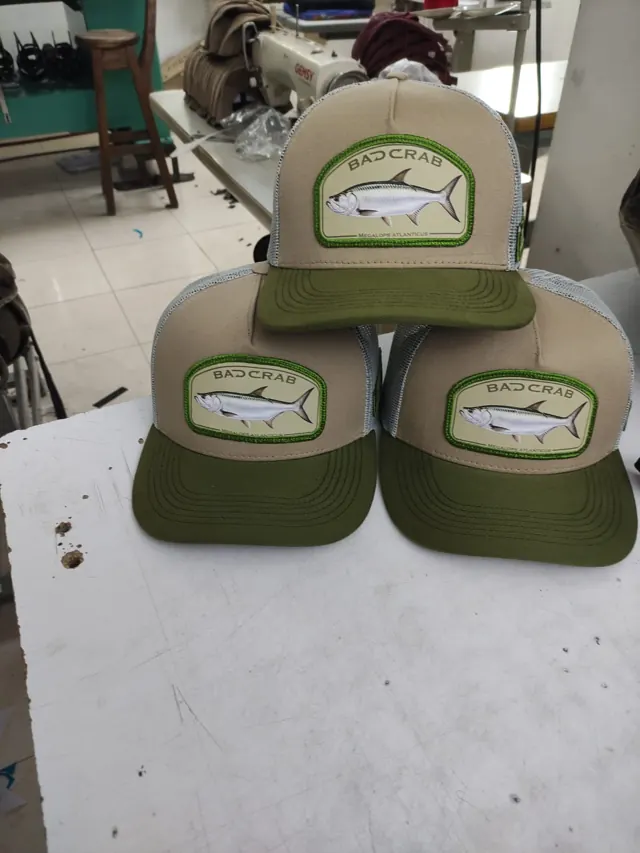 Tres gorras trucker con parche de sábalo real, corona beige, malla gris y visera verde oliva