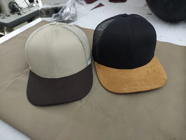 Dos gorras trucker lisas, una beige con visera café y otra negra con visera en gamuza