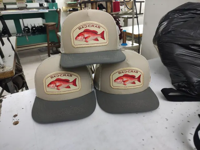 Gorras trucker con parche de pargo cubera sobre la mesa del taller