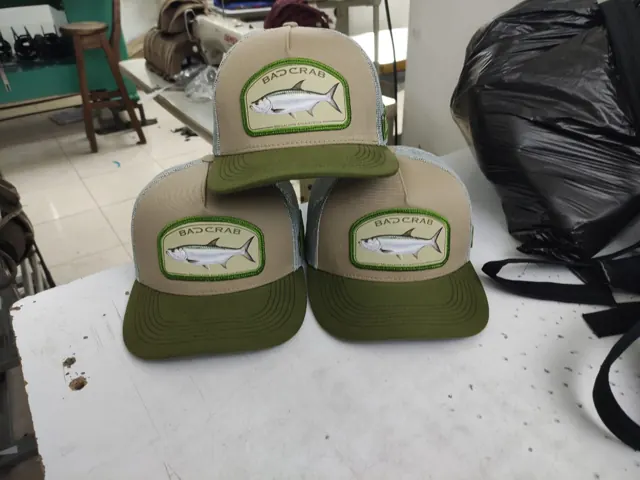Tres gorras trucker con parche de sábalo real sobre la mesa del taller